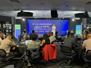Sală de conferință cu participanți la mese, în timpul unui keynote