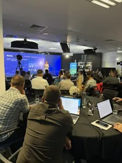 Participanți cu laptopuri urmărind prezentarea de pe ecranul mare